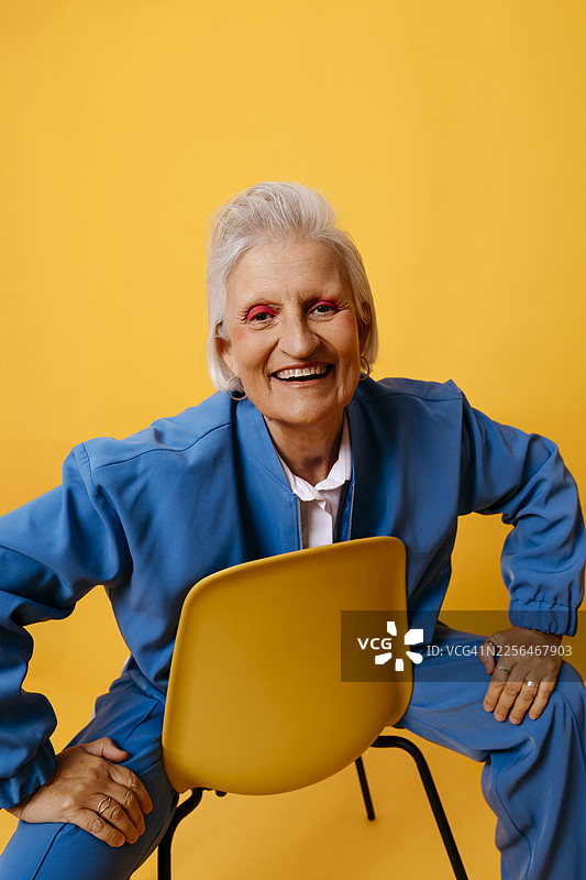 身穿蓝色西装的女子坐在椅子上，对着黄色背景微笑图片素材