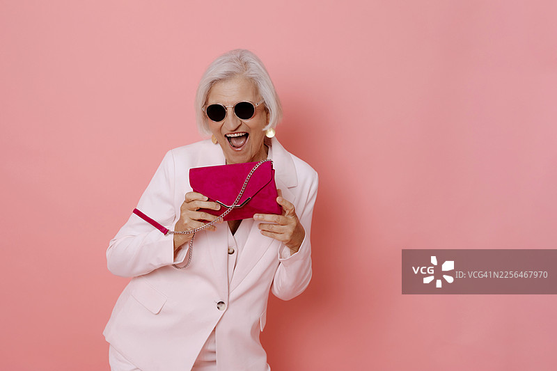 身穿白色西装、戴着太阳镜、手拿粉色手提包的快乐女子，背景为粉色图片素材