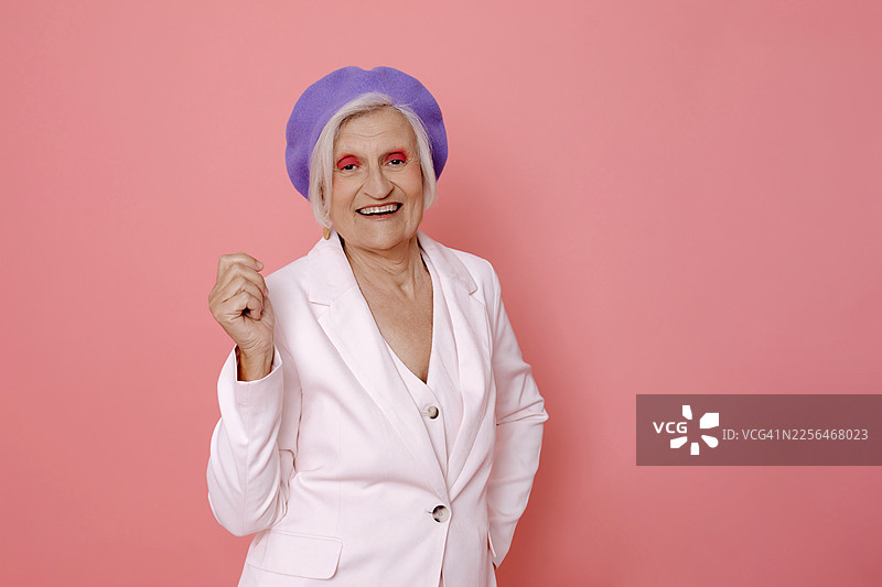 身穿白色西装和紫色贝雷帽的快乐女子在粉色背景前微笑图片素材