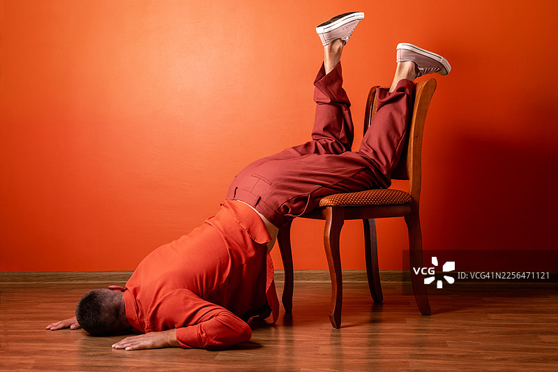 一名穿着橙色西装、精疲力尽的男子在室内椅子上因职业倦怠而瘫倒图片素材