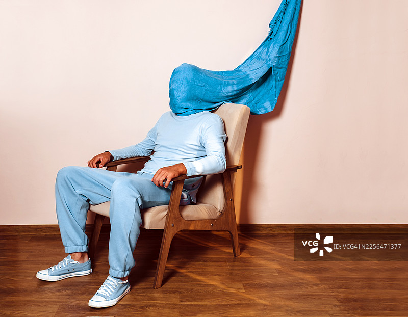 穿着蓝色衣服、头部被遮住的男人坐在扶手椅上，表情悲伤图片素材