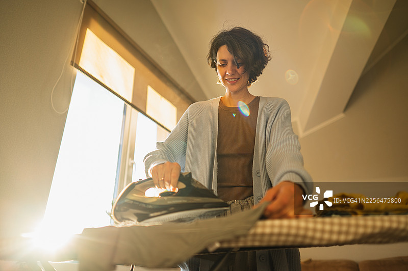 阳光下，一名女子在家中进行日常熨衣活动图片素材