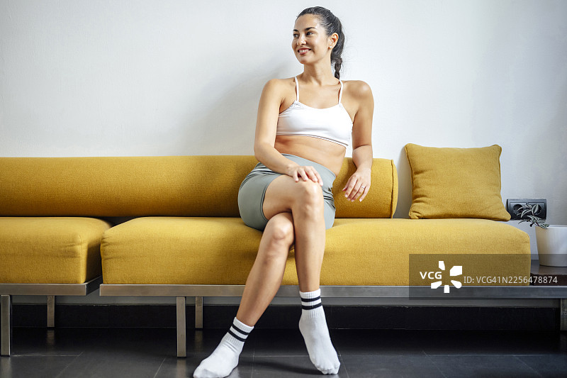 身着运动服的女性在健身训练后，在黄色沙发上放松图片素材
