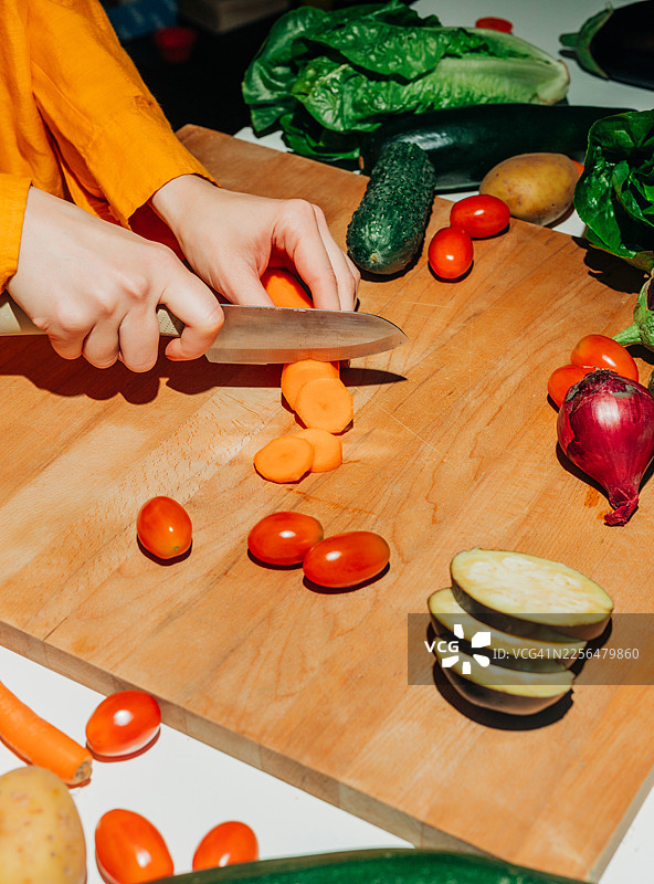 女士用刀在厨房的桌子上切胡萝卜，准备制作健康的沙拉图片素材