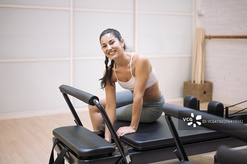 一位微笑着的人形教练在锻炼后坐在健身房的普拉提器械上图片素材