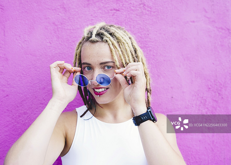 戴眼镜的卷发女子微笑着在粉色墙前摆姿势图片素材
