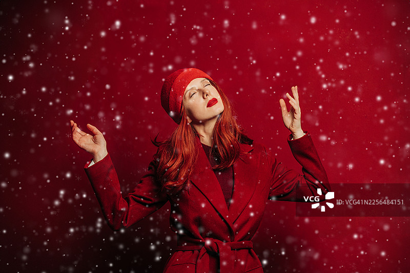 身穿红色外套的时尚女性，在圣诞氛围中享受飘落的雪花图片素材