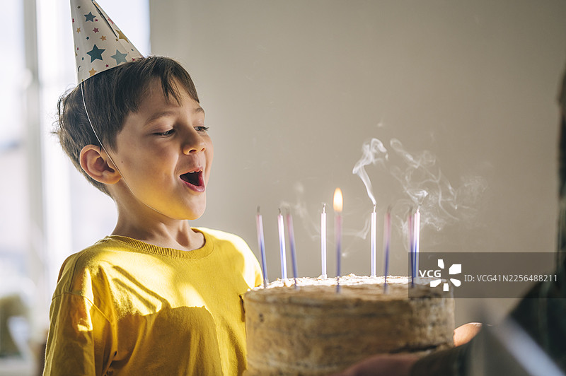 戴着派对帽的孩子快乐地吹灭生日蛋糕上的蜡烛图片素材