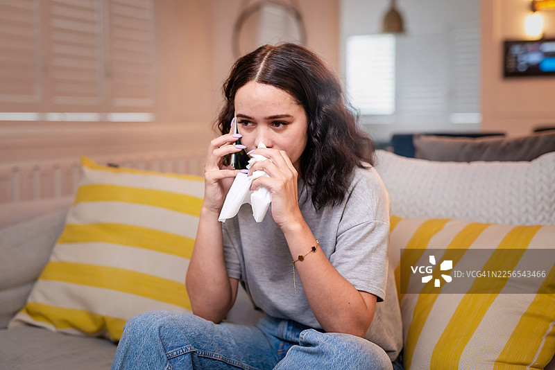 生病的女人在家里的沙发上咳嗽，手边放着纸巾和鼻腔喷雾图片素材