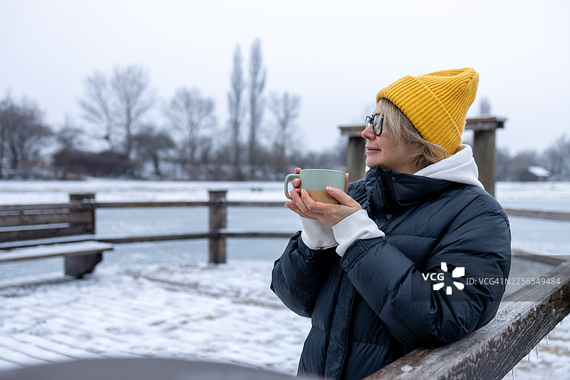 一位宁静的女子在冰封的冬日湖边享用热饮。图片素材