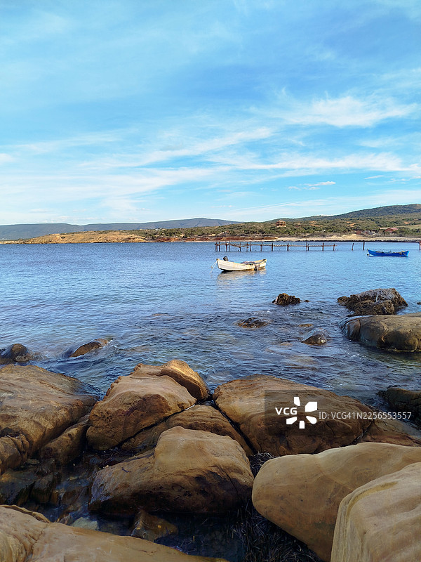 宁静的海滨风光，有船只和岩石海岸，蓝天下的景色图片素材