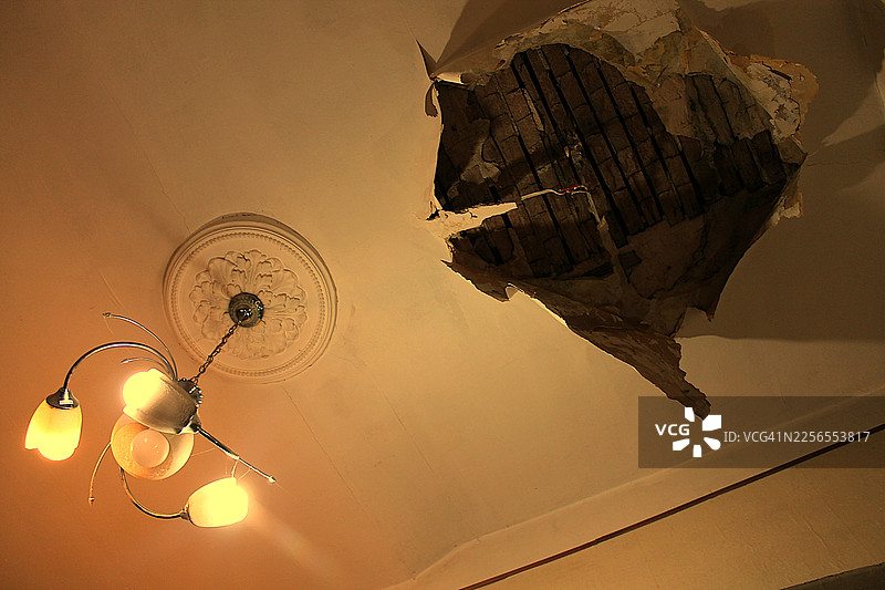 受损的天花板有一个大洞，露出结构元素，下方悬挂着一盏复古吊灯，灯光温暖图片素材