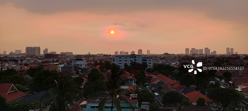 日落时分广阔城市景观的高角度视图，建筑物的剪影映衬着充满活力的橙粉色天空，印度尼西亚雅加达图片素材