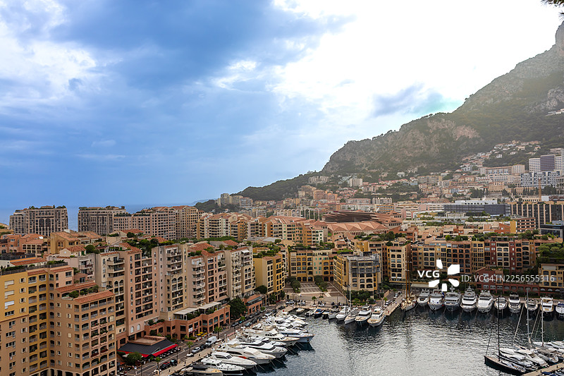 蒙特卡洛，摩纳哥，人口稠密的沿海城市，拥有繁华的码头和雄伟的山脉背景，天空多云，航拍视角，摩纳哥图片素材