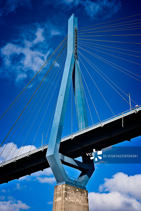 从低角度拍摄的现代悬索桥，背景是充满活力的蓝色天空和零星的云彩，突显了建筑的坚固和设计。德国汉堡。图片素材
