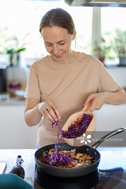 快乐的女人在她明亮的厨房里用新鲜蔬菜烹饪健康餐食图片素材