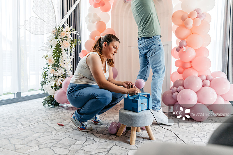 中年男女用充气泵给气球打气，并把它们挂起来准备生日派对图片素材