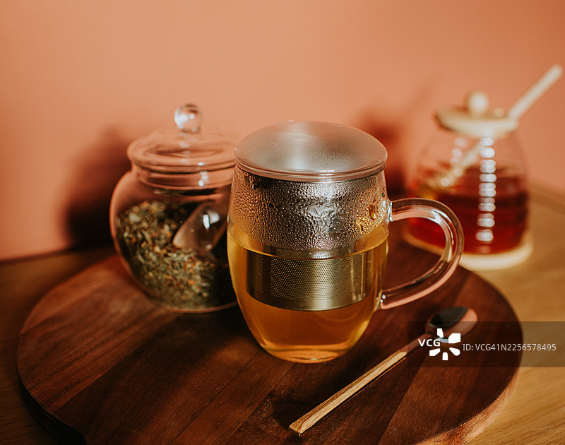 带内置滤网的玻璃茶杯和琥珀色茶水，放在木质托盘上。图片素材