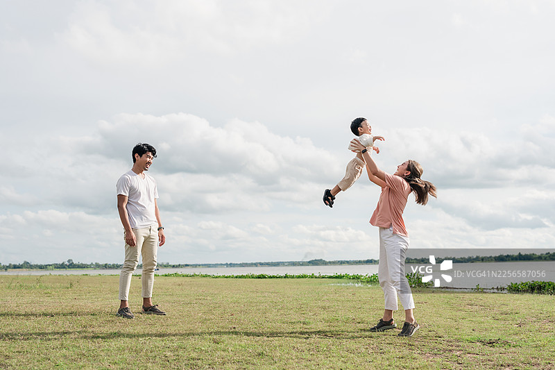 亚洲家庭户外玩耍，母亲高高举起飞翔的幼儿儿子，父亲微笑着看着，亲情连接，充满爱的感情，无忧无虑的家庭生活方式图片素材