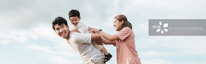 亚洲家庭在湖边自然公园户外活动，享受亲子时光。父亲背着儿子，母亲支持着孩子，充满爱意、快乐和幸福的休闲活动，周末活动。图片素材