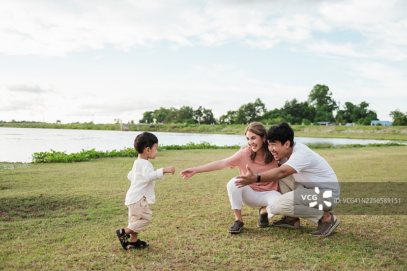 亚洲家庭在草地上迎接蹒跚学步的儿子。父母面带微笑，张开双臂，亲情，爱的情感，人寿保险，团结，幸福，一家三口。图片素材