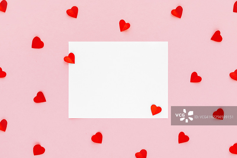 情人节背景。粉色背景上的空白贺卡和红色心形纸屑。情人节创意概念。俯视，平面布置图片素材