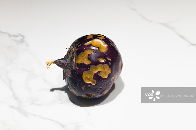 烤紫茄子放在白色大理石台面上，带有烤焦的外皮和茄蒂，艺术美食呈现图片素材