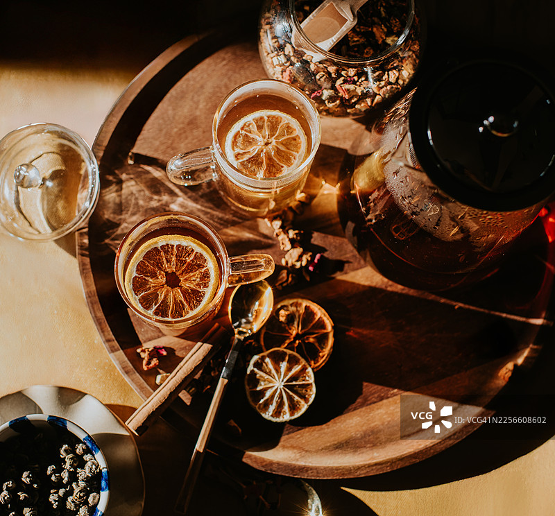 俯视木质托盘上放着两杯草本茶，旁边有干柑橘片。图片素材