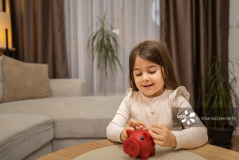 小女孩在家里的红色储蓄罐里存钱图片素材