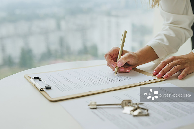 在桌上的钥匙和剪贴板上签署房地产协议的手图片素材