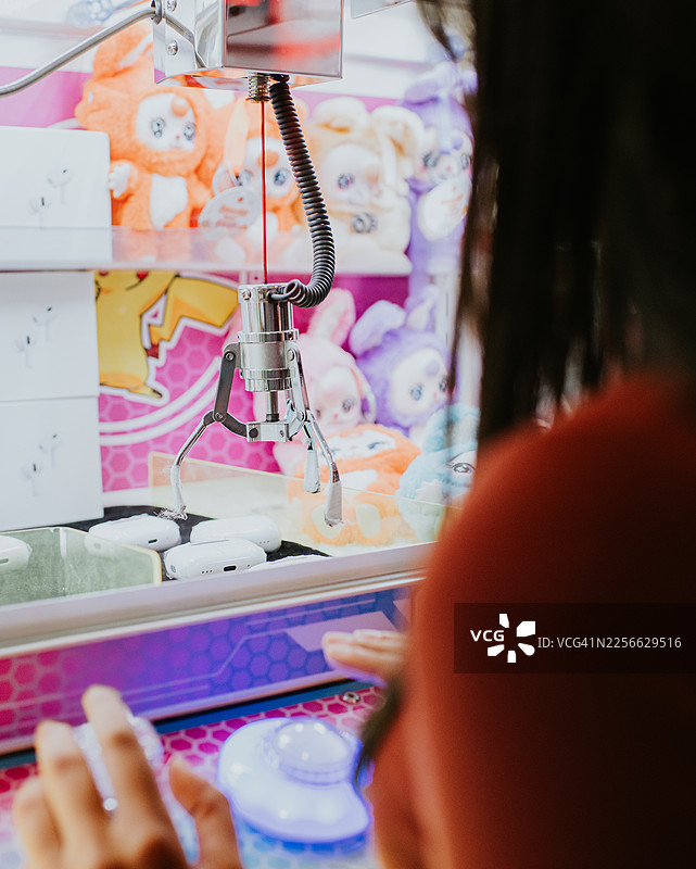 明亮的街机厅内，玩家操控着抓娃娃机，爪子伸向奖品，特写镜头。图片素材