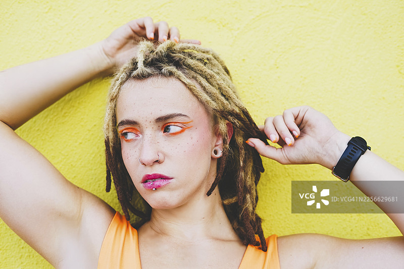 留着脏辫、戴着穿孔饰物的女子在黄色墙壁前摆姿势图片素材