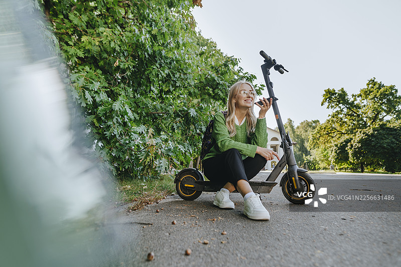 穿着商务装的女性在户外坐在电动滑板车上使用智能手机图片素材