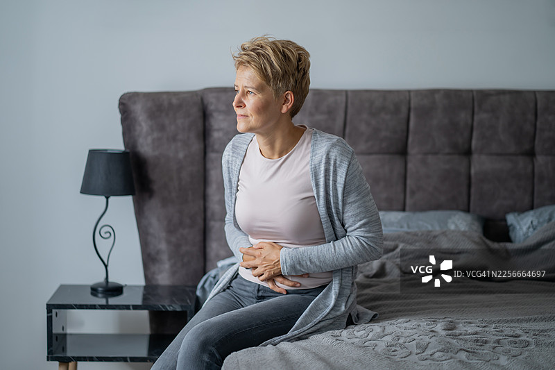 一名女子在家中坐在床上，忍受着胃痛图片素材