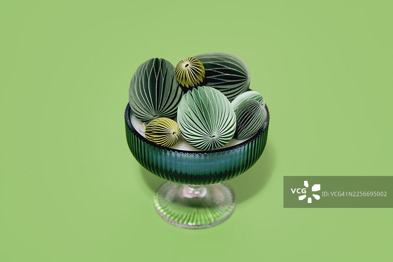 纸艺复活节彩蛋放在罗纹玻璃花瓶中，背景为亮绿色，俯视角度。图片素材