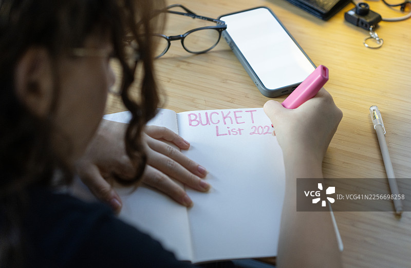 孩子在书桌上用笔记本写下2026年人生愿望清单，旁边有智能手机和文具图片素材