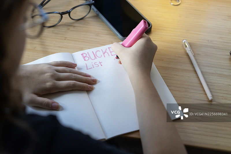 孩子在书桌上用笔记本写下2026年愿望清单，旁边有智能手机和文具图片素材