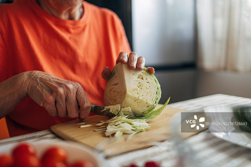 一位年长的女性正在切菜板上切新鲜卷心菜，准备健康的餐食图片素材