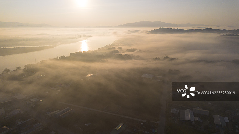 泰国清莱府清盛县湄公河边境，在浓雾笼罩下，柔和的光线逐渐显露出河道弯曲和城镇风光的高处视角。图片素材