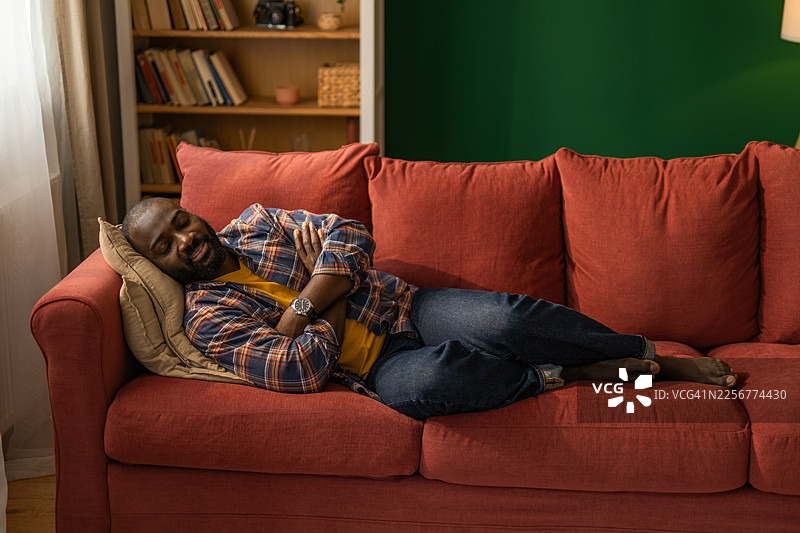 男人惬意地躺在红色沙发上，在家中享受宁静的小憩图片素材