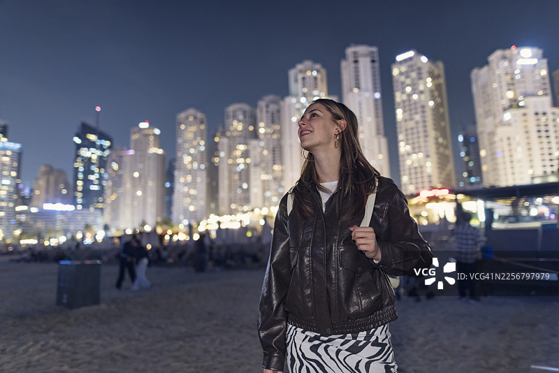 夜色中，年轻女子漫步在迪拜码头的沙滩上。图片素材