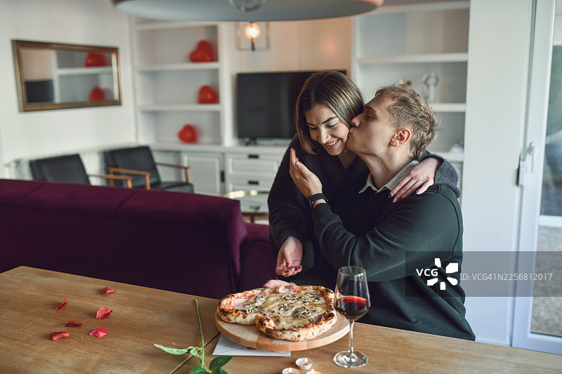 浪漫情侣在家中舒适的客厅里，在情人节分享披萨并亲吻图片素材
