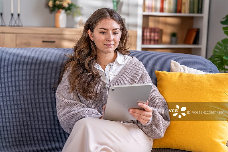 年轻女子舒适地躺在沙发上使用平板电脑图片素材