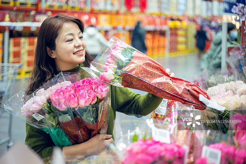 一位中年亚洲女性正在超市里挑选花卉。图片素材