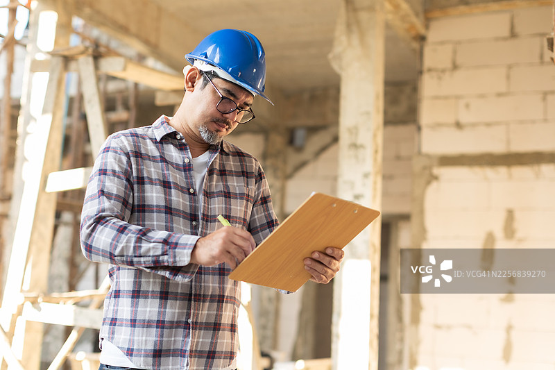 建筑工地上的建筑经理和亚洲工程师正在用笔记本电脑监督工程进展。身穿安全背心和头盔的亚洲工程师正在检查结构元素。图片素材