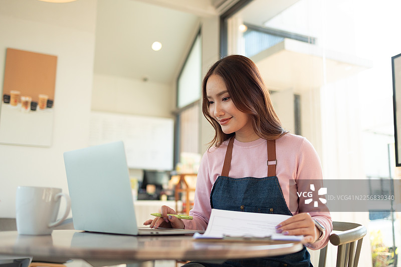 建筑工地现场，一位建筑经理和一位亚裔工程师正在用笔记本电脑监督建筑进展。亚裔工程师身穿安全背心和头盔，正在检查结构构件。图片素材