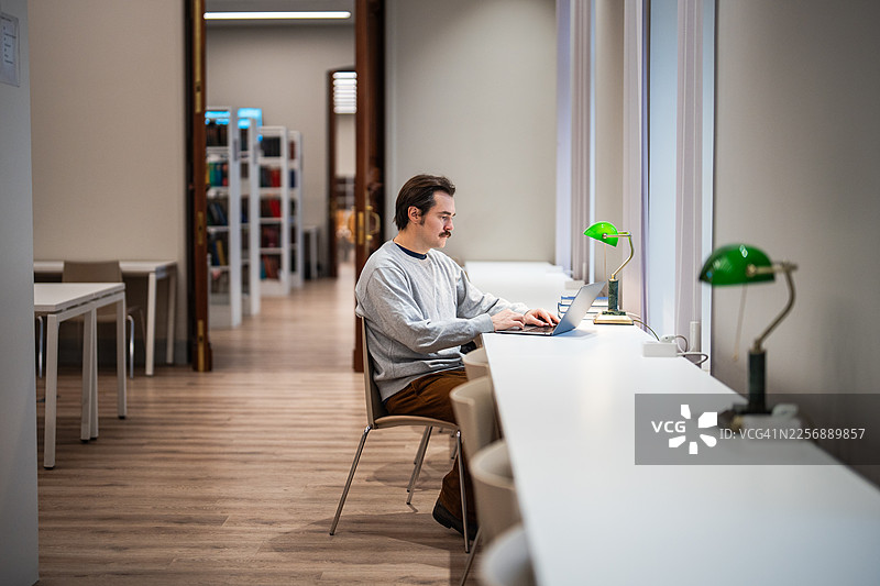 专注的成熟男学生在大学图书馆用笔记本电脑学习，获取新知识，攻读第二学位。图片素材
