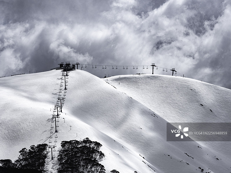 暴风雨云层笼罩着积雪覆盖的山脉和滑雪场图片素材