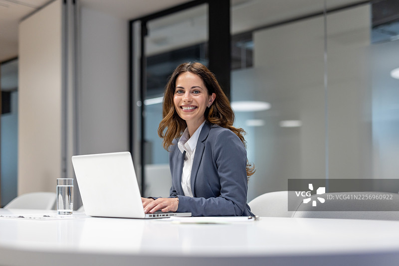 一位女商人在现代办公室里微笑着使用笔记本电脑工作图片素材