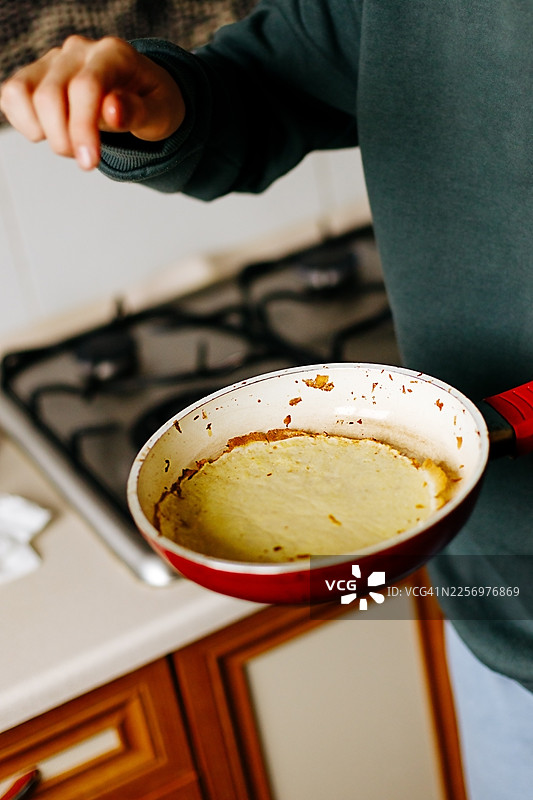 一个人在厨房里拿着一个红色的煎锅，锅里正煎着薄饼图片素材